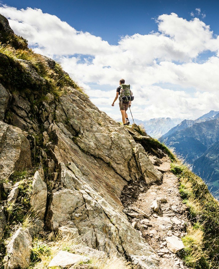 Auf dem Weg zum Gipfel Wanderer steht auf einem felsigen Weg mit Blick auf die Berge und den Himmel.